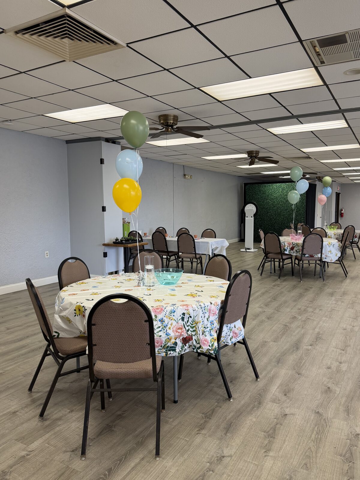 Round tables with floral linens and balloon bundles, boxwood wall behind